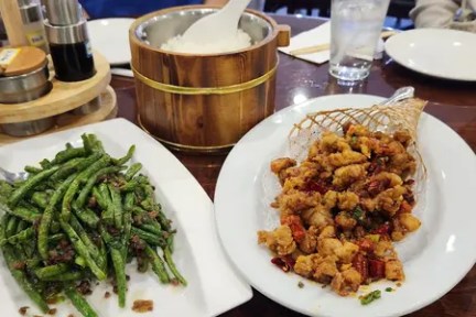 Plates of green beans and fried chicken on a table with a rice bowl.