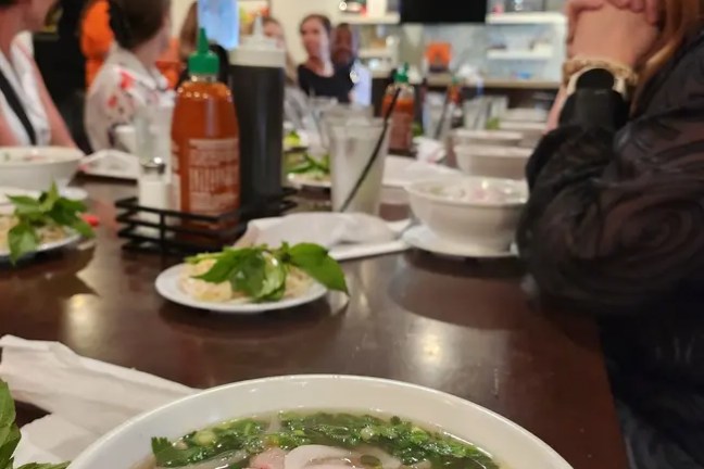 People dining in a restaurant with bowls of pho on the table.