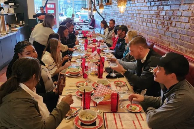 Group of people dining at a restaurant with a long table and checkered tablecloth.