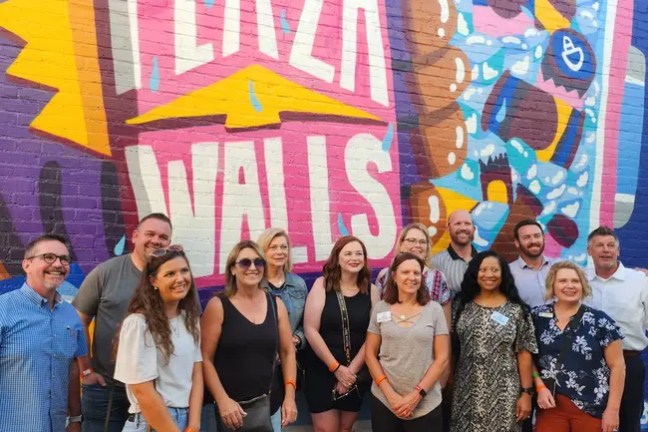Group of people smiling in front of a colorful mural.