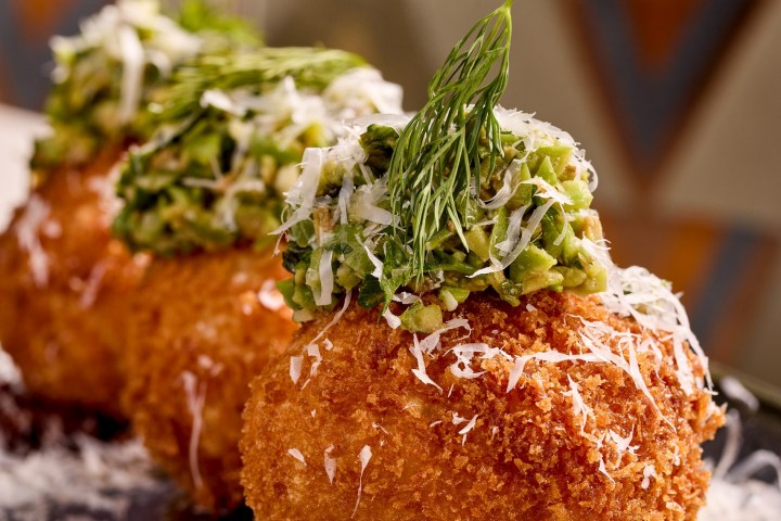 Three arancini balls garnished with herbs on a plate.