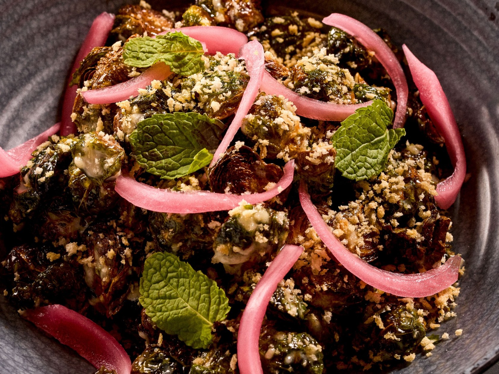Bowl of brussels sprouts with pickled onions and mint leaves.