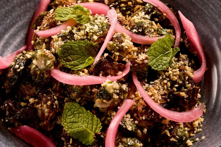 Bowl of brussels sprouts with pickled onions and mint leaves.