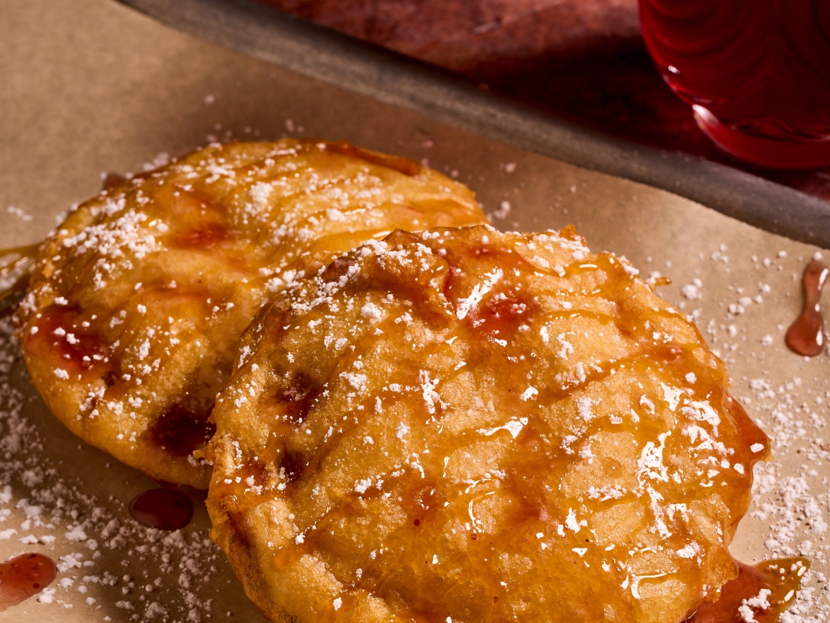 Two fried pancakes with syrup and powdered sugar on a tray.