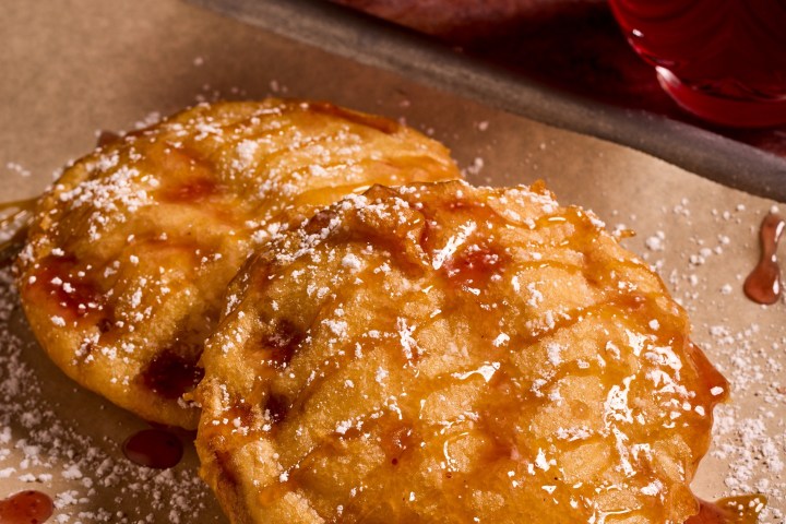 Two fried pancakes with syrup and powdered sugar on a tray.