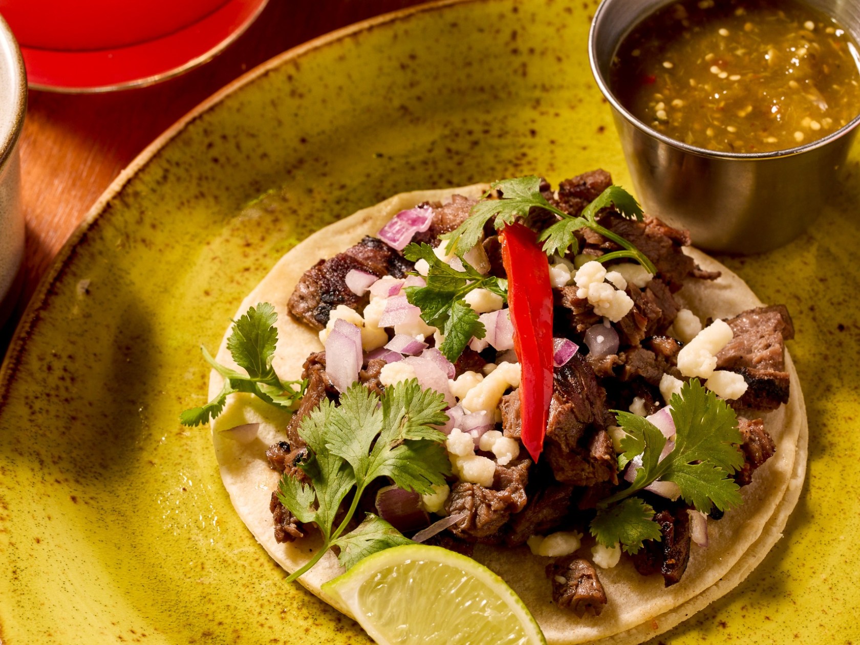 Taco with meat, onions, cilantro, and lime on a green plate, salsa on the side.