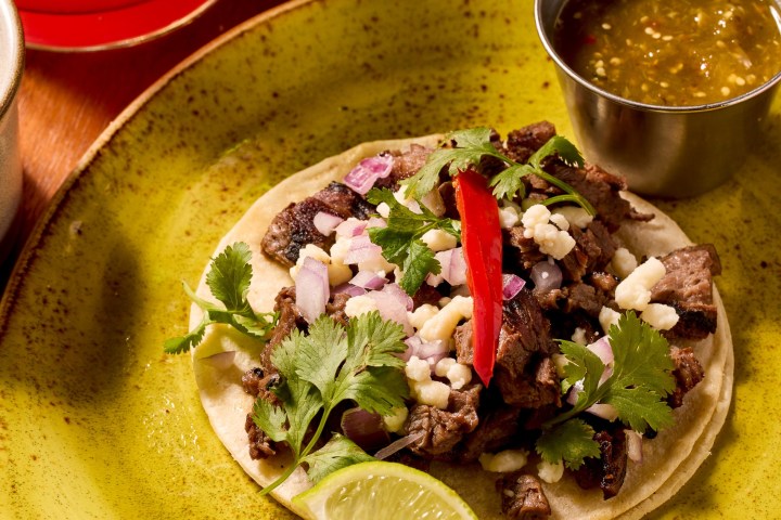 Taco with meat, onions, cilantro, and lime on a green plate, salsa on the side.