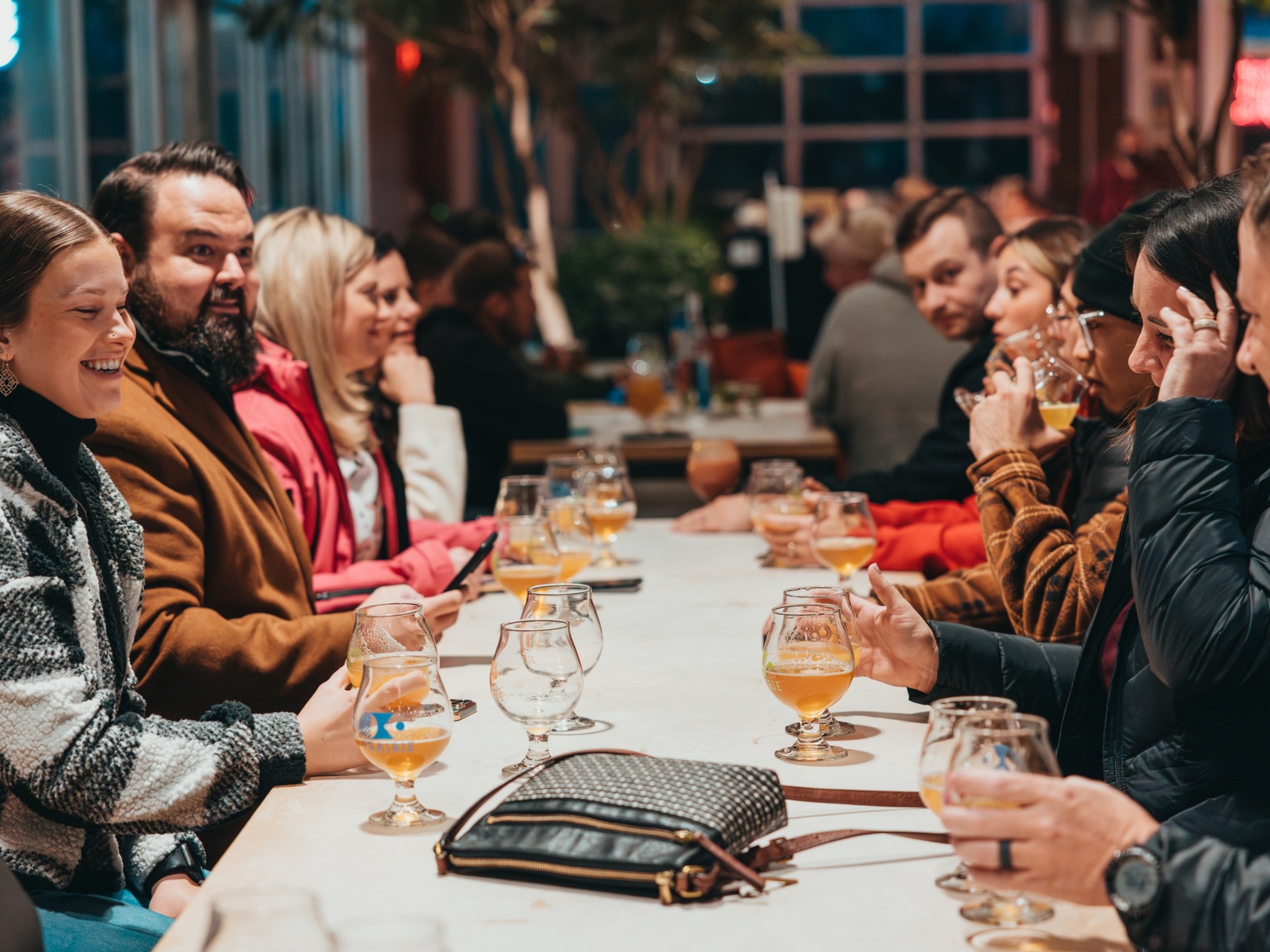 Group of people sitting at a long table with drinks in a lively indoor setting.