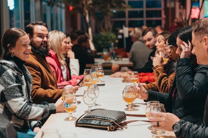 Group of people sitting at a long table with drinks in a lively indoor setting.