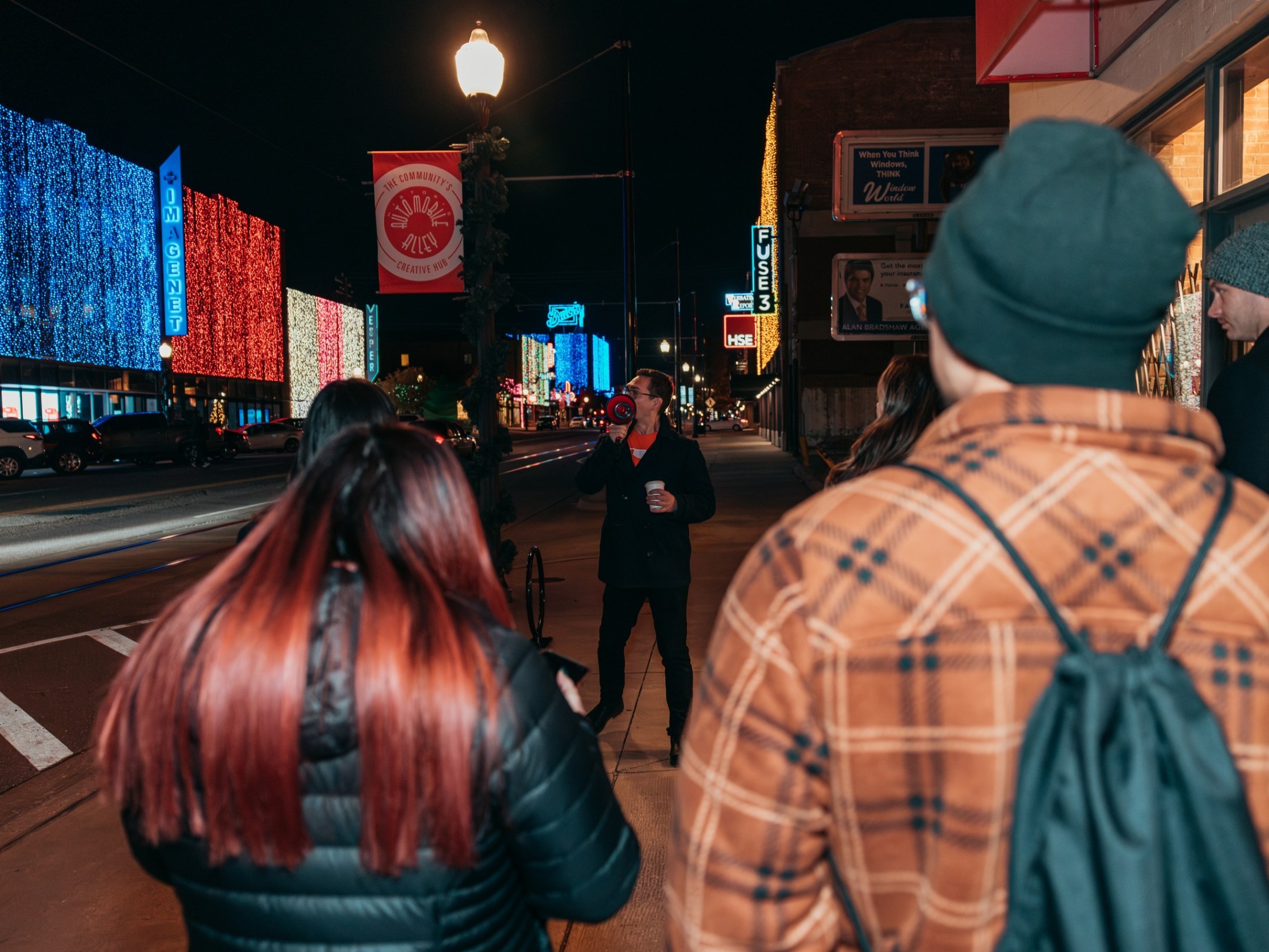 People walking on a lit city street at night, colorful building lights in the background.