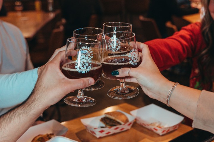 Four hands toasting with beer glasses over food in a restaurant.