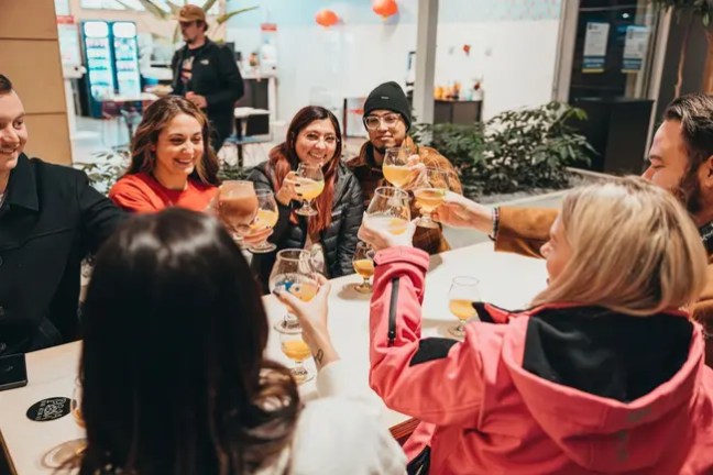 Group of people sitting around a table, clinking glasses and smiling.